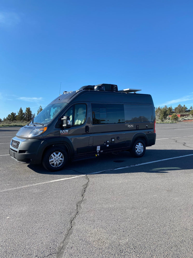 overlooking a stormy ocean with distant rocky islets under a grey sky.|Explore with this dark grey Ram ProMaster RV rental. This Rize camper van offers adventure travel — photo 5