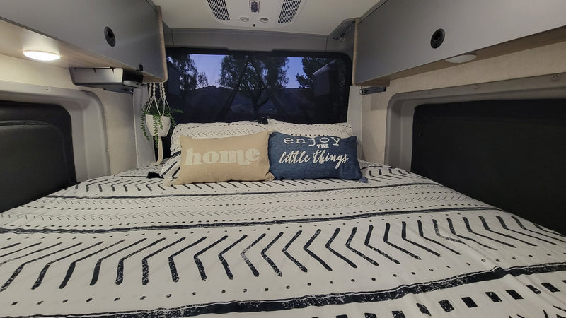 Cozy RV rental bed with black & white patterned bedding, 'home' & 'enjoy the little things' pillows, & overhead cabinets. — photo 9