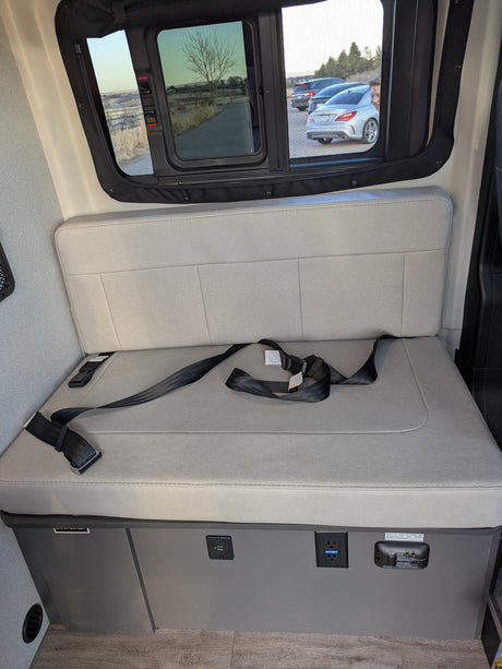 Comfortable RV rental interior: bench seat with seatbelts, power outlets & scenic window views for your journey.