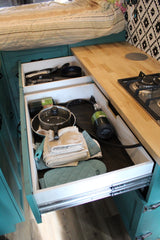RV rental: Open kitchen drawers reveal cookware, towels, and propane tanks, next to a stove on a wood counter.