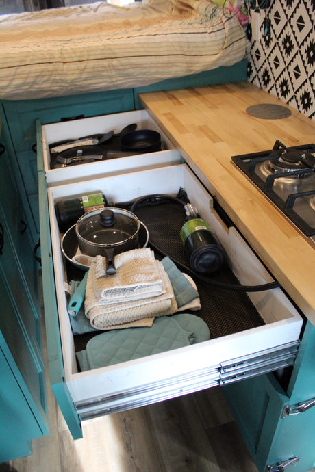 RV rental: Open kitchen drawers reveal cookware, towels, and propane tanks, next to a stove on a wood counter.