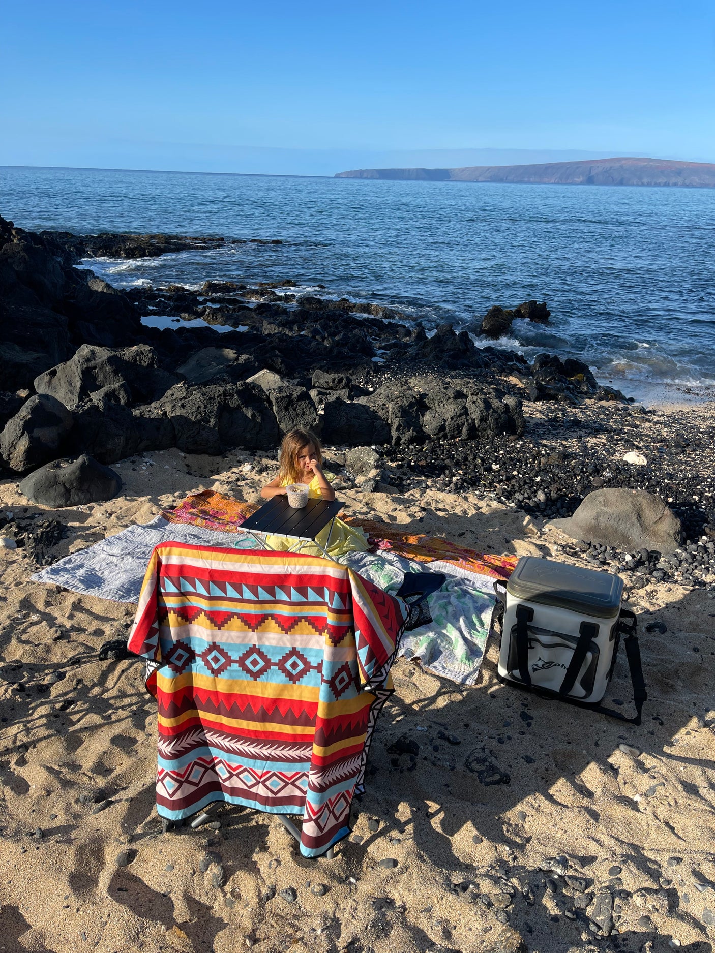 Secluded beach picnic scene, perfect after an RV rental adventure, showing a child, blankets, and a cooler by the ocean.