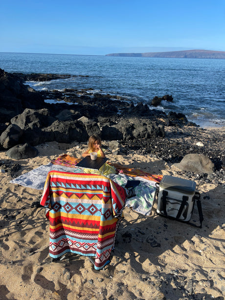 Secluded beach picnic scene, perfect after an RV rental adventure, showing a child, blankets, and a cooler by the ocean.