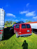 A red van with a roof box and an RV are parked on vibrant green grass under a clear blue sky. Great for an rv rental trip!