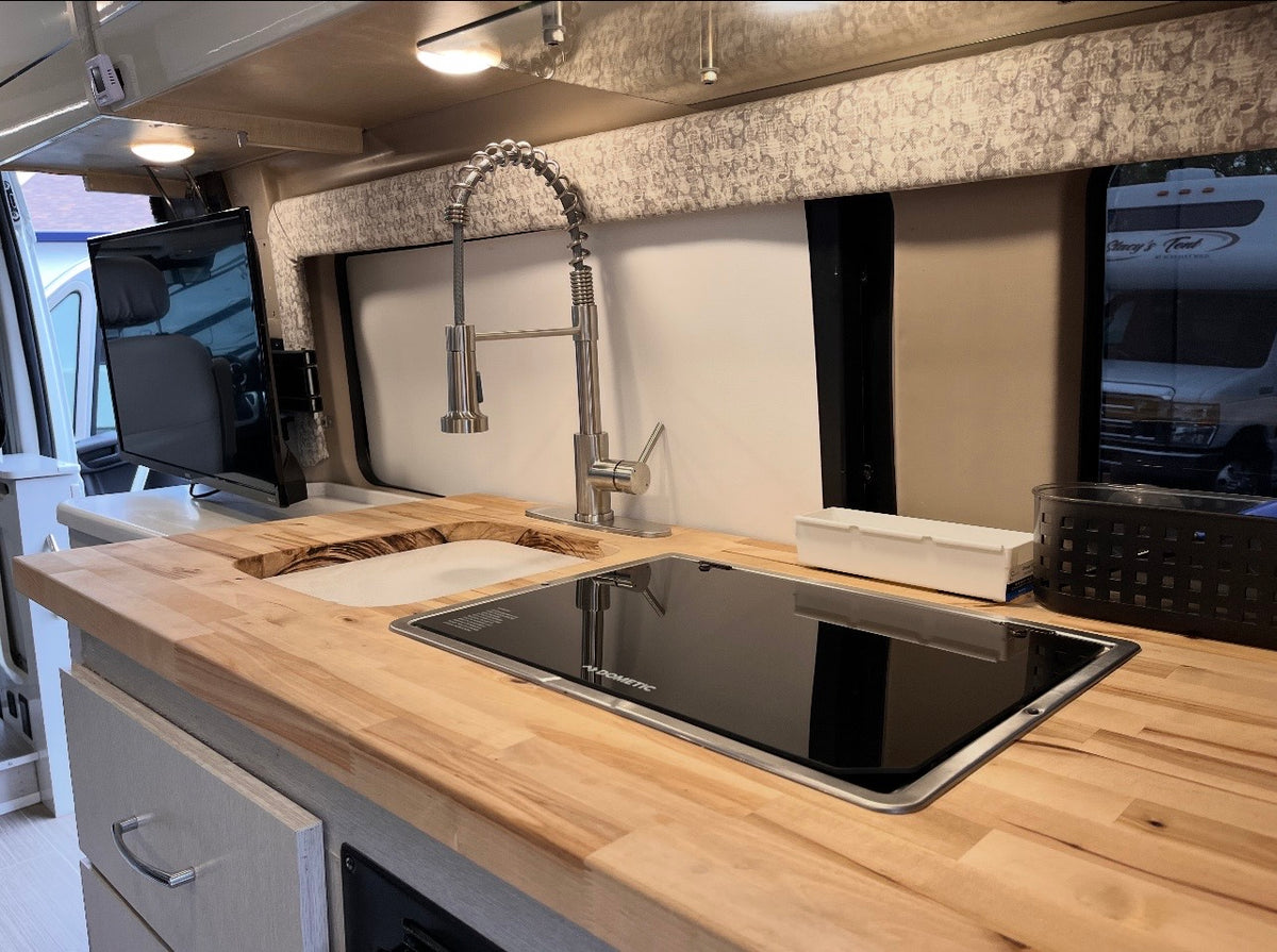 RV rental kitchen: a light wood countertop, modern faucet, integrated sink, Dometic cooktop, and a mounted TV. — photo 4