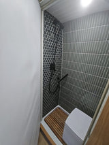 This RV rental features a sleek, compact shower with black and grey tiles, wooden mat, and portable toilet.