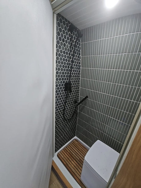 This RV rental features a sleek, compact shower with black and grey tiles, wooden mat, and portable toilet.
