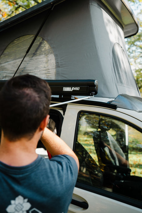Man adjusting a pop-top RV rental campervan with a Fiamma awning, parked outdoors. Ready for adventure.