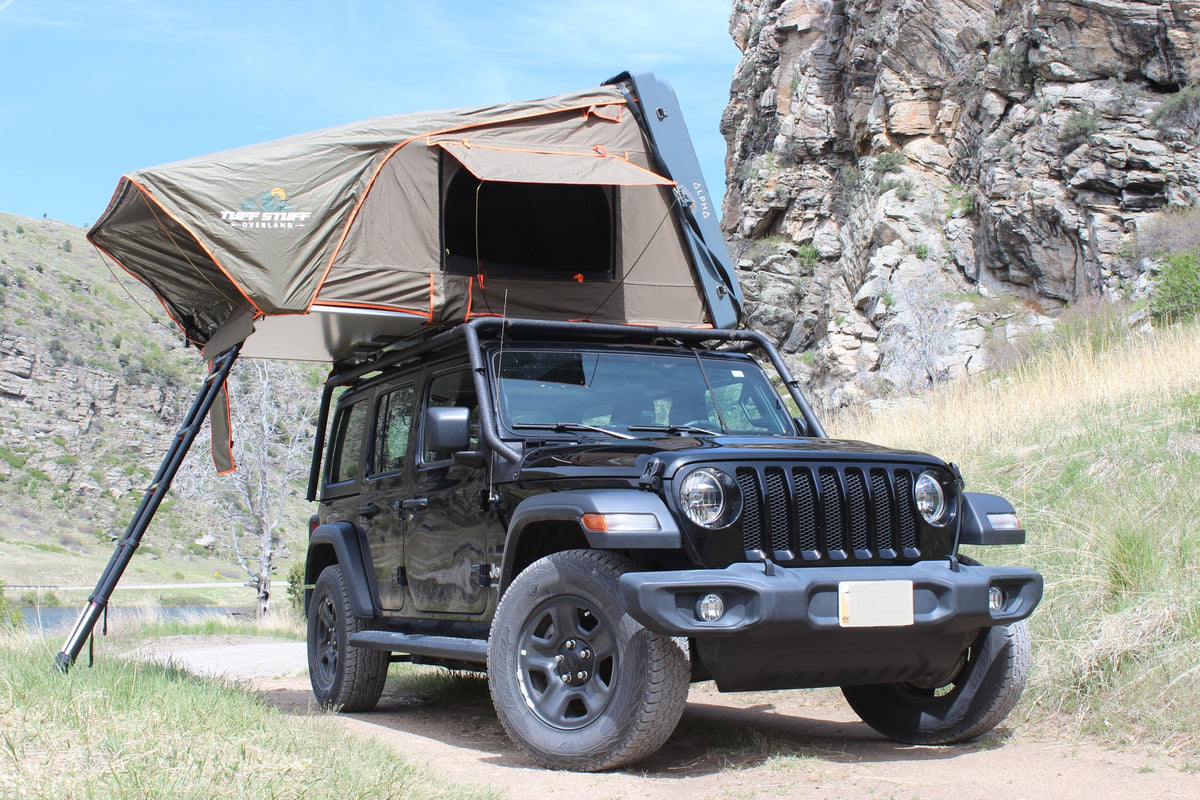 An rv rental black Jeep Wrangler with an open Tuff Stuff overland rooftop tent, ready for camping in a rocky, grassy landscape.