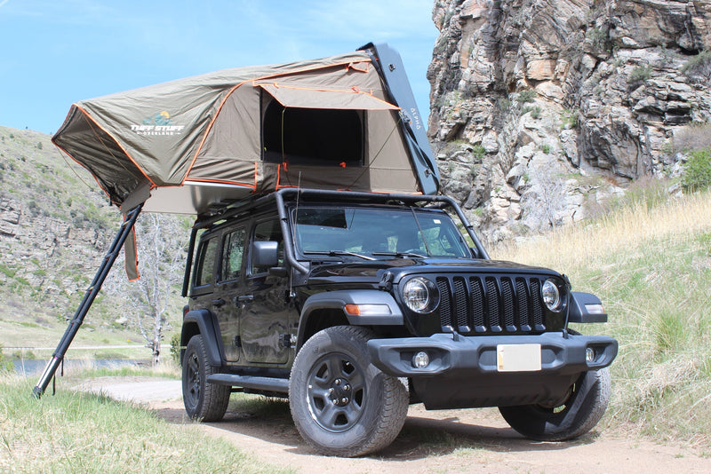 An rv rental black Jeep Wrangler with an open Tuff Stuff overland rooftop tent, ready for camping in a rocky, grassy landscape. — photo 1