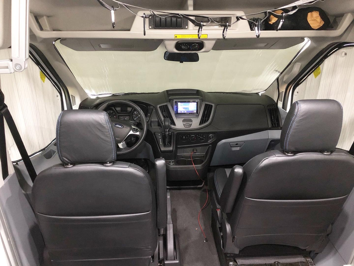 Spacious RV rental van interior, showing two dark front seats, the dashboard, and a sunshade on the windshield.