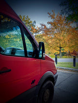 Vibrant red Sprinter van, ideal for rv rental travel, parked with autumn trees in the background under a daytime sky.