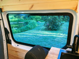RV rental interior with wood accents, a sink, and a large window overlooking a peaceful lake and lush green landscape.