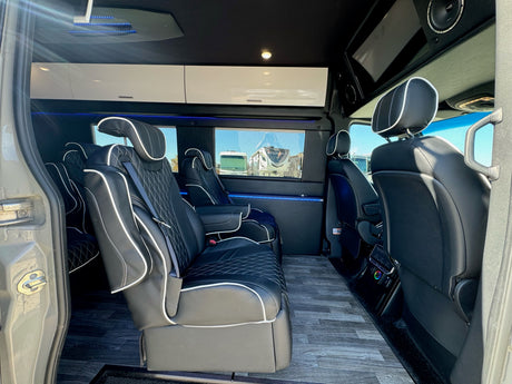 Luxury RV rental interior: spacious van with black leather captain's chairs, wood-look floor, and ambient blue LED lighting.