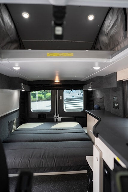 RV rental camper van interior. Features a large bed, counter, windows, and bright lighting. Ideal for road trips & adventures. — photo 8