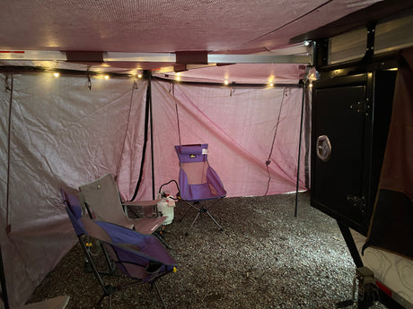 Spacious interior of an RV rental annex with camping chairs, string lights, and a gravel floor for outdoor comfort.