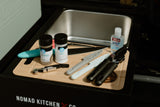 Portable kitchen essentials for your RV rental: Spices, tools, and hand sanitizer on a cutting board, part of a Nomad Kitchen setup.