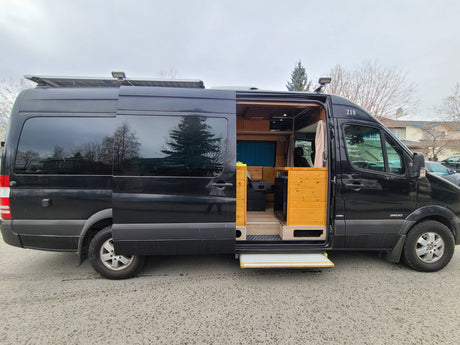 Black Mercedes Sprinter van, ready for rv rental, with custom wood interior, solar panels, and extended step.
