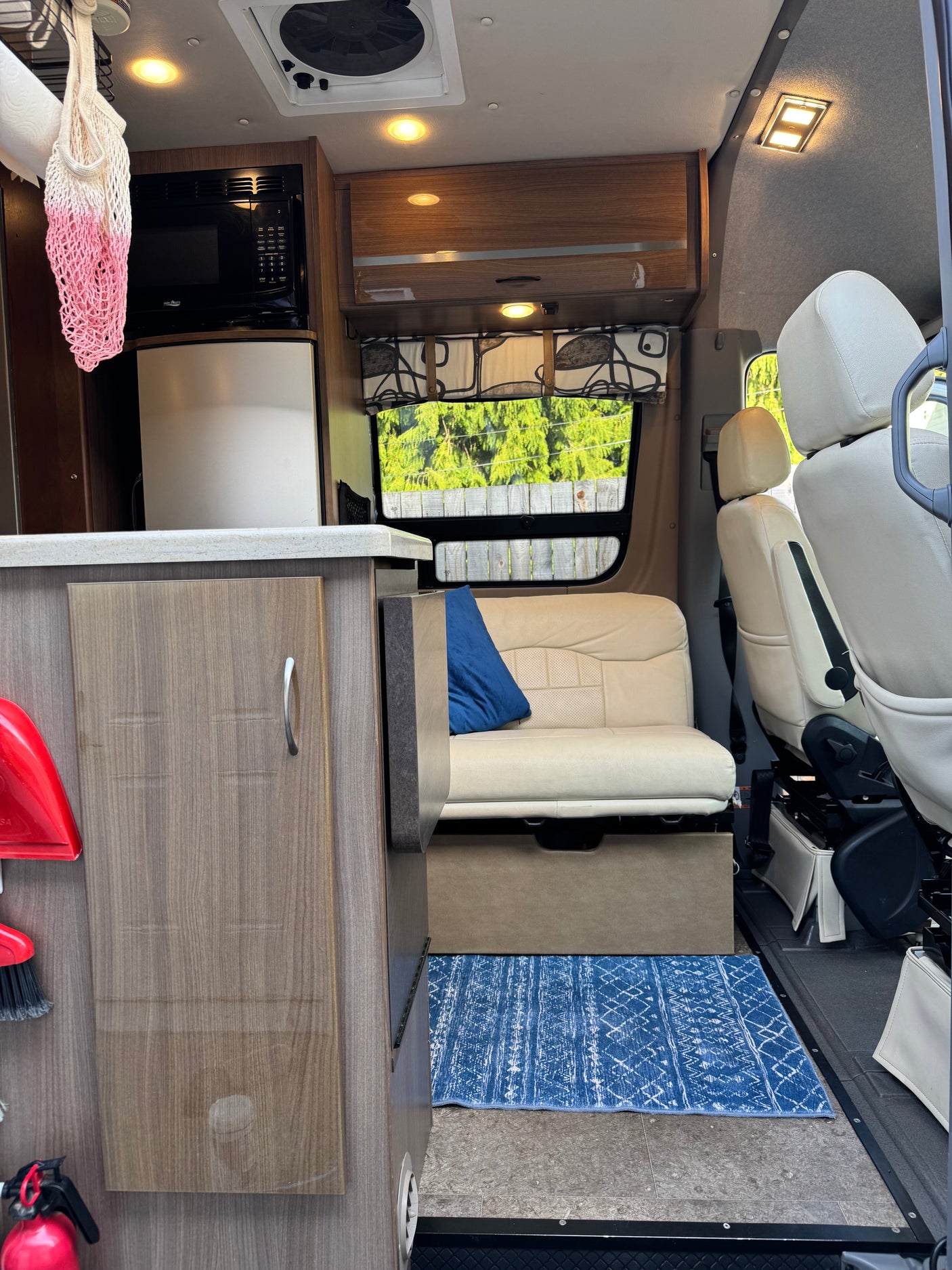 This RV rental interior features a compact kitchen with appliances, a cozy sofa with a blue pillow, and front seats. Ideal for mobile living.