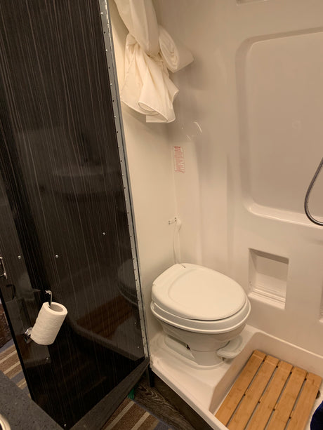 RV rental's compact wet bath features a toilet, shower, and bamboo floor mat, optimizing space for travel convenience.