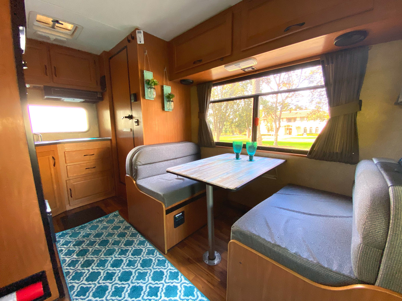 Cozy RV rental interior with a dinette, kitchen area, and a large window view, highlighted by a teal patterned rug.