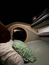 Cozy RV rental interior at night. The full moon shines through the roof opening, illuminating a comfortable bed with a green pillow.