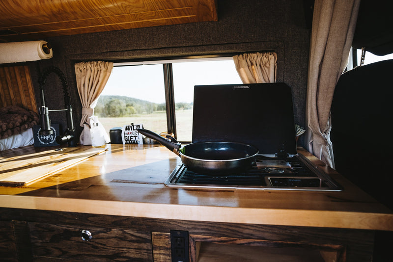 Experience van life in this RV rental's functional camper kitchen with a Dometic stove, sink, wooden counter, and scenic view. — photo 10