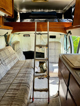 Cozy RV rental interior featuring a ladder leading to an overhead bunk, sofa seating, and a compact kitchen counter.