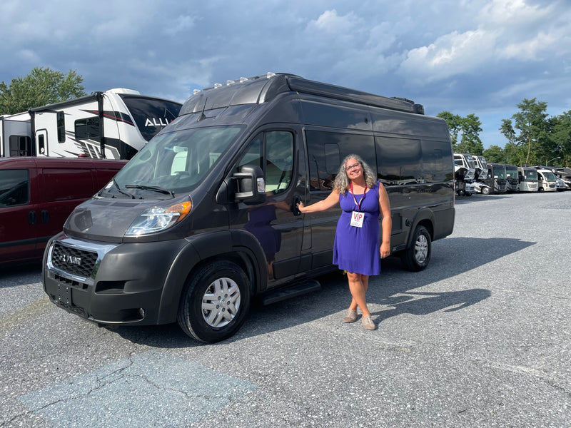 Exploring RV rental options! A woman smiles by a grey camper van at an RV show, with many motorhomes visible. — photo 4