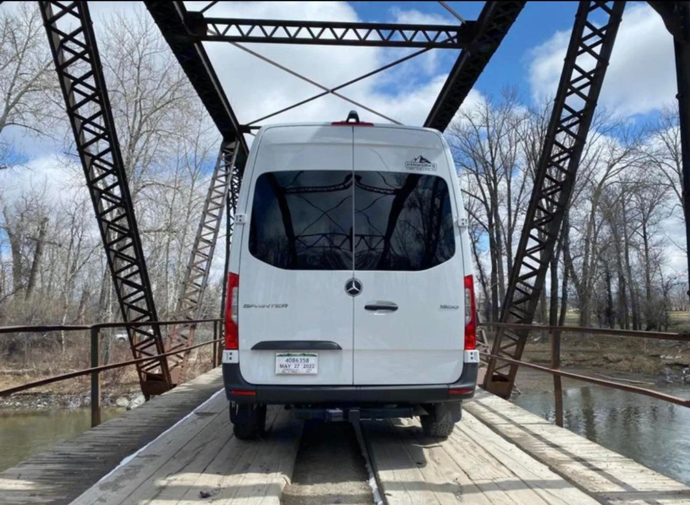  and windows showing a snowy landscape.|White Sprinter van RV rental on a rustic wooden bridge over a river with bare trees. Ready for adventure!|White Mercedes Sprinter RV rental parked on a rustic truss bridge over a river — photo 7