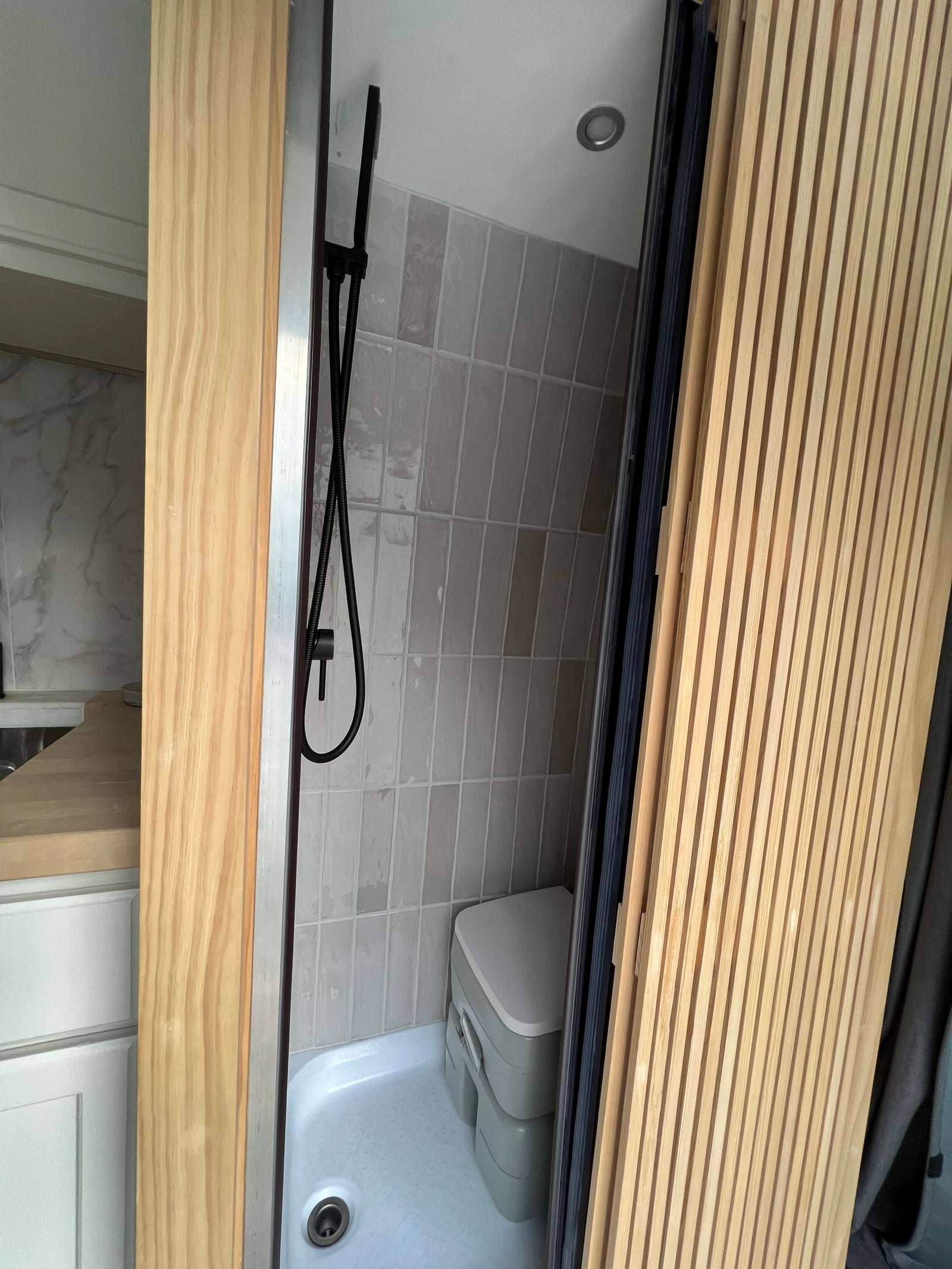 An RV rental features a compact wet bath with black shower, grey tiled walls, and a portable composting toilet.