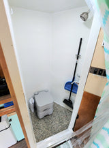 RV rental: Compact white bathroom with shower, portable toilet, and cleaning tools. Efficient, small space.