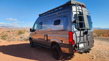 Gray Revel rv rental camper van with roof rack & ladder, parked in a scenic desert landscape with mountains.