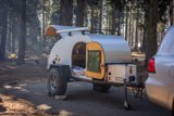 Teardrop RV rental at a forest campsite. This off-road ready trailer has an outdoor kitchen & comfy sleeping area.