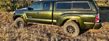 Olive green Toyota Tacoma pickup with camper shell off-road in dry grass. Great for an rv rental adventure!