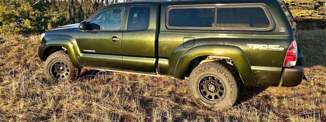 Olive green Toyota Tacoma pickup with camper shell off-road in dry grass. Great for an rv rental adventure!