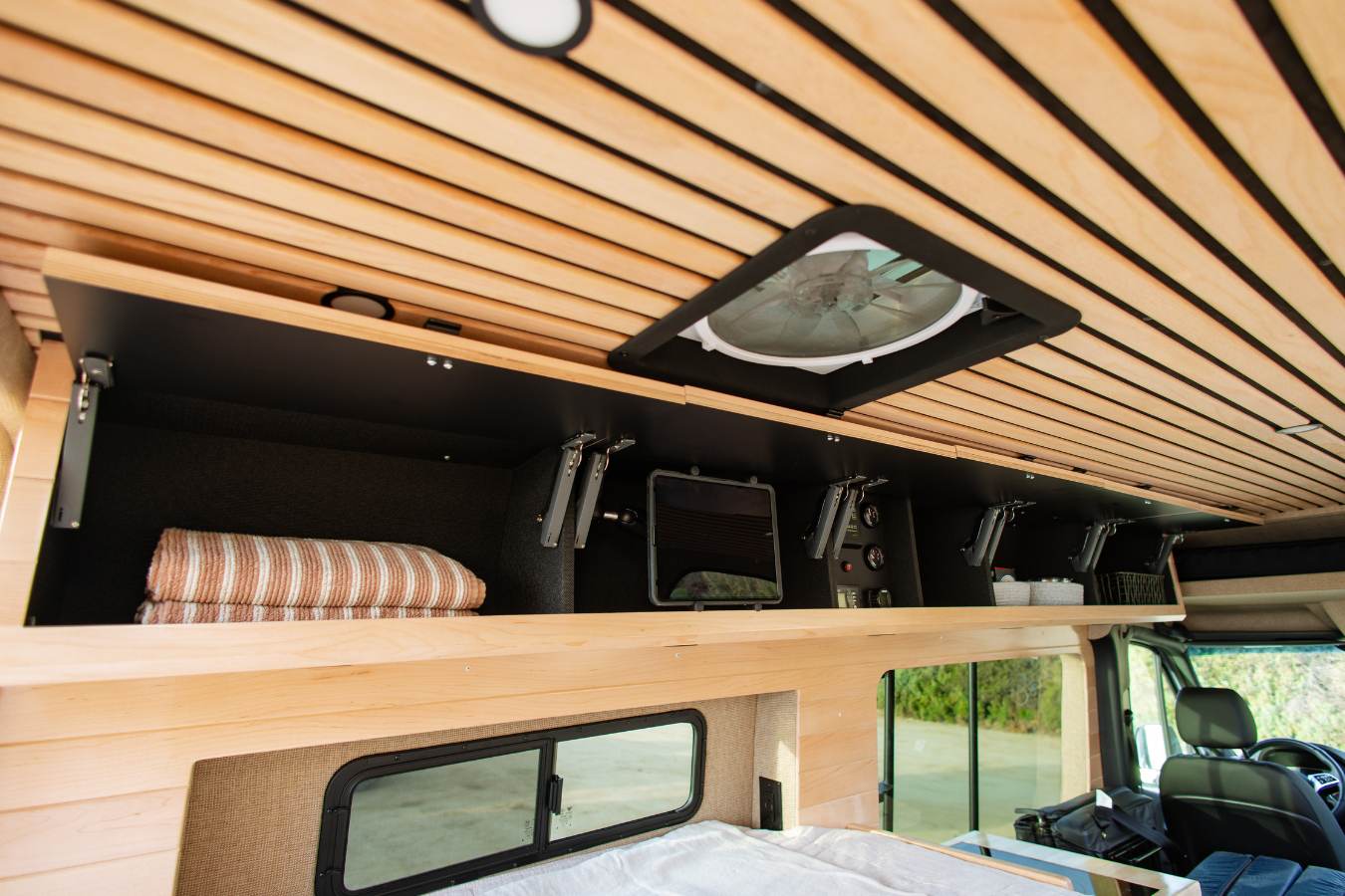 RV rental interior: overhead storage, fan, and controls set against a warm, slatted wooden ceiling. Bedding ready for travelers.