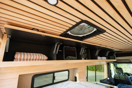 RV rental interior: overhead storage, fan, and controls set against a warm, slatted wooden ceiling. Bedding ready for travelers.