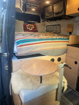 An inviting rv rental interior featuring a striped bed, round table, cozy seating, and smart storage solutions.