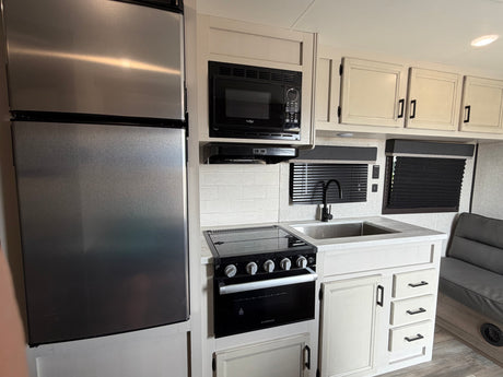 Compact rv rental kitchen: stainless fridge, black microwave, oven, sink, and modern light cabinets with dark hardware.