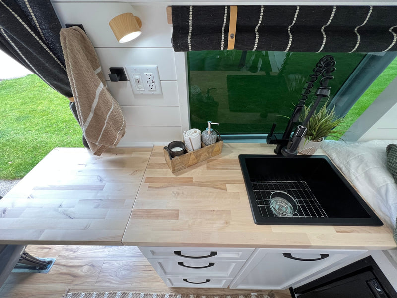 RV rental van interior with modern kitchenette, sink, countertop, and a cozy bed visible on the right. — photo 13