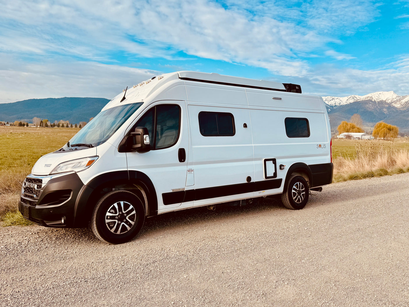 White Winnebago Solis camper van on gravel, mountains behind. Explore freedom with this RV rental.