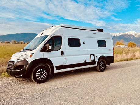 White Winnebago Solis camper van on gravel, mountains behind. Explore freedom with this RV rental.