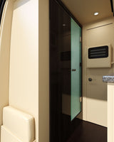 Compact bathroom and plush seating inside a modern RV rental, featuring a frosted glass shower door and wood accents.