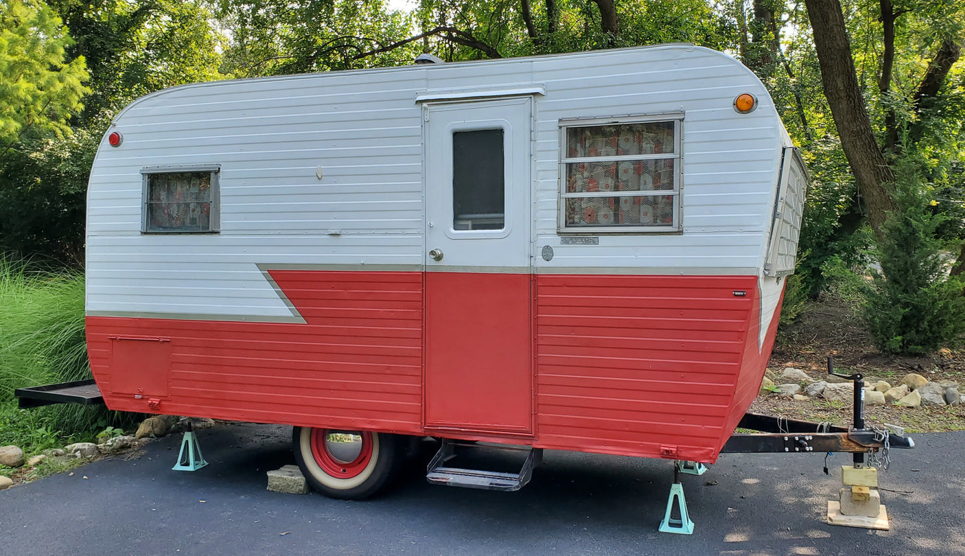 This vintage red and white travel trailer is a classic RV rental option, parked under green trees.