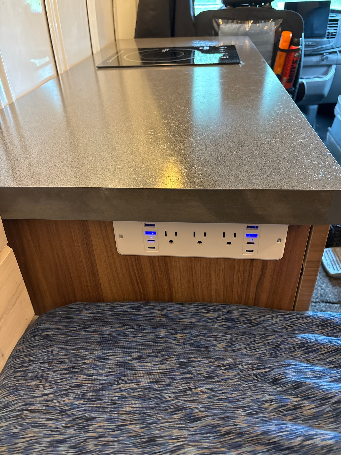 RV rental kitchen: counter with induction cooktop, AC outlets, & glowing blue USB ports for charging devices.