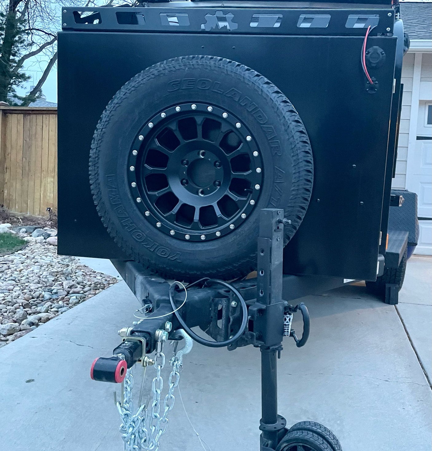 This black, rugged off-road trailer, a versatile RV rental option, features a spare tire, roof rack, and trailer jack. Ready for adventure.