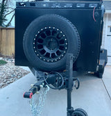 This black, rugged off-road trailer, a versatile RV rental option, features a spare tire, roof rack, and trailer jack. Ready for adventure.