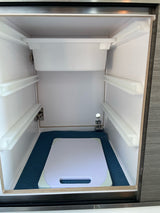 RV rental interior: Clean, empty storage space with white rails, a top bin, and a cutting board on a blue mat.