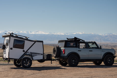 Explore with an RV rental! This Ford Bronco tows a TigerMoth overland trailer with mountain views, perfect for adventure.